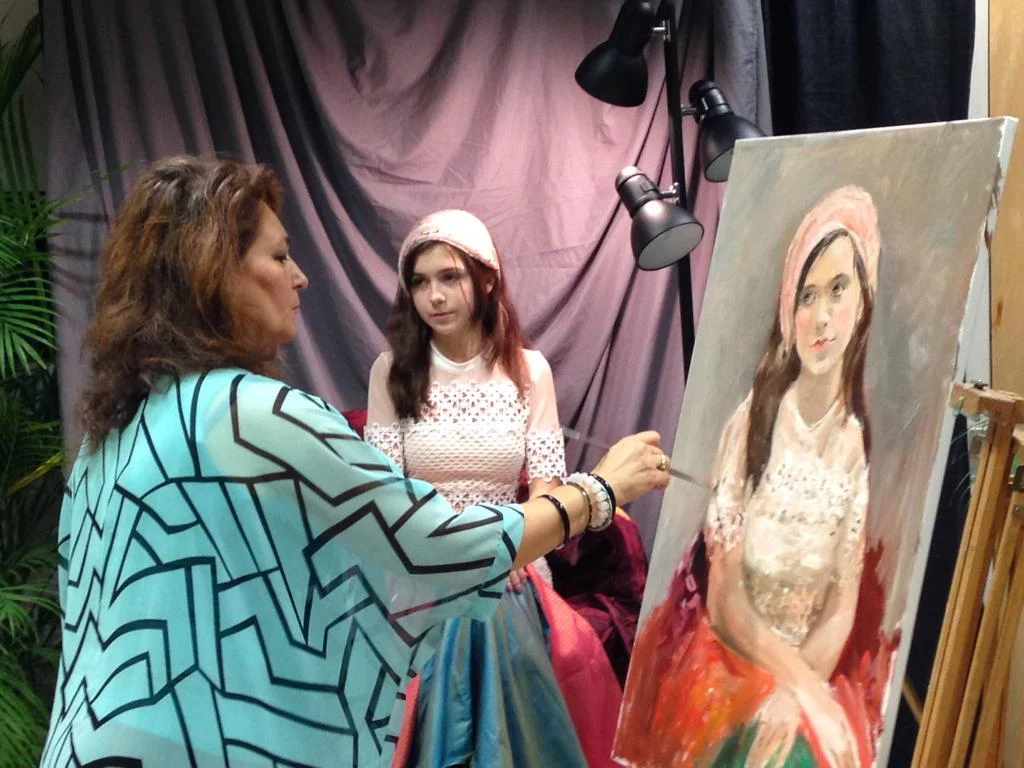 An artist painting a young sitter during a live portrait session