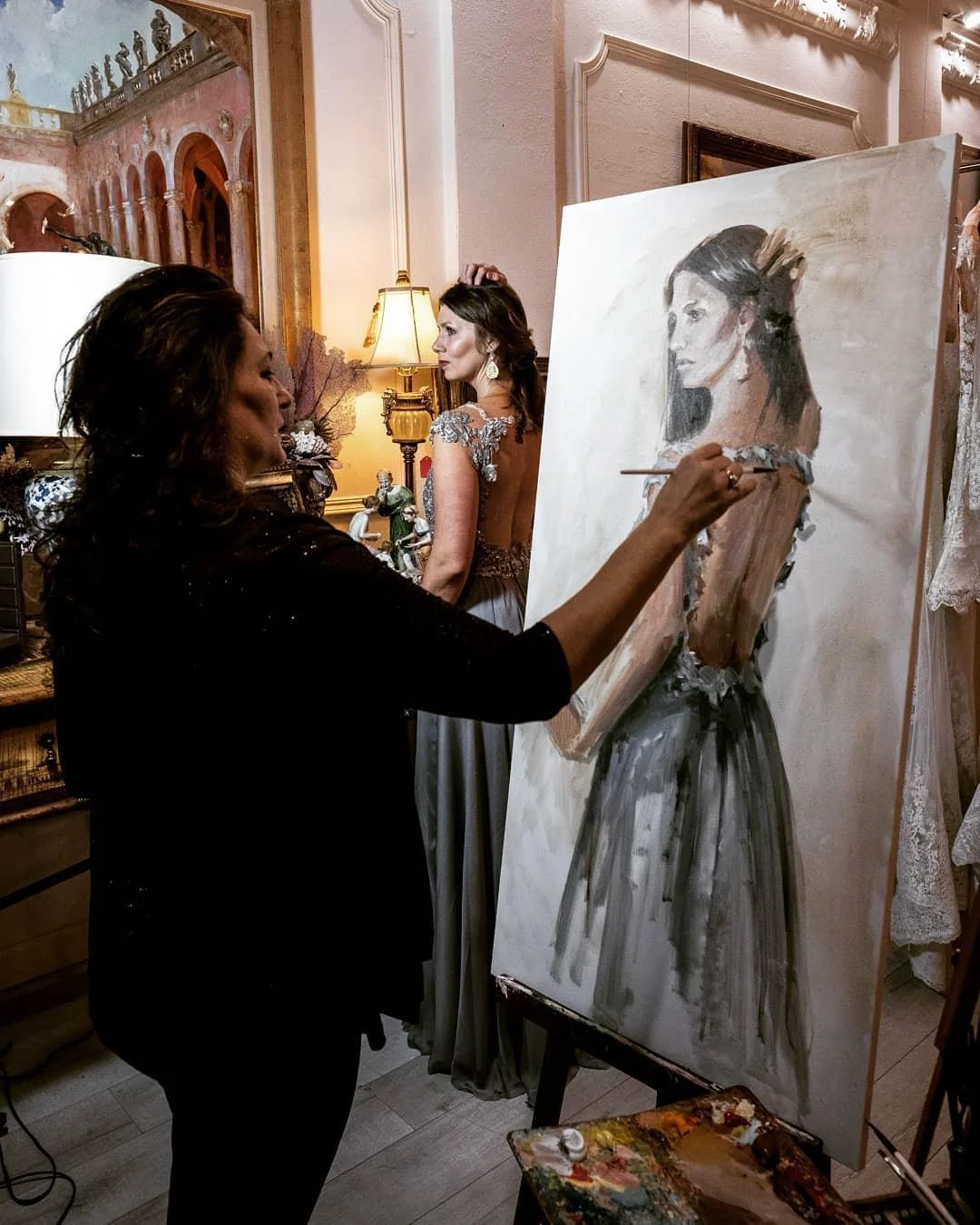 Violetta painting a portrait at the easel with the sitter posing behind the canvas