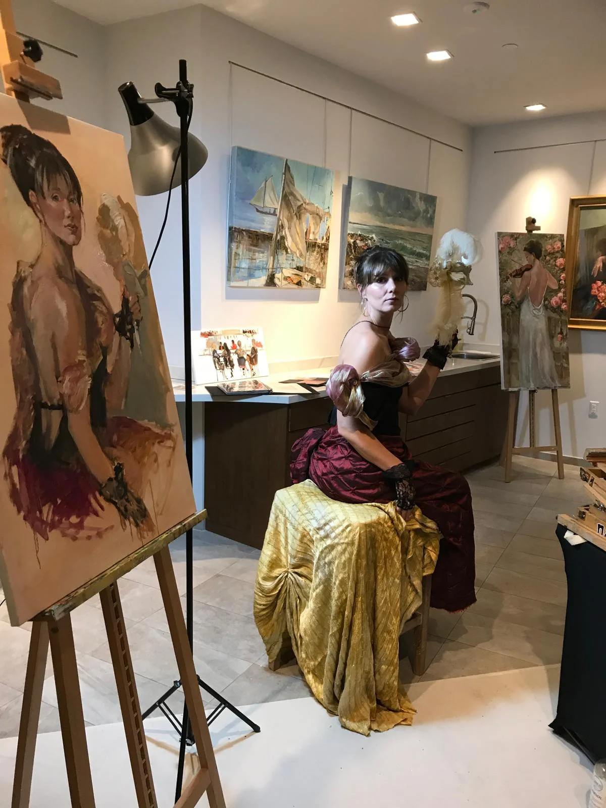 A sitter holding a feathered mask beside her unfinished portrait in the studio